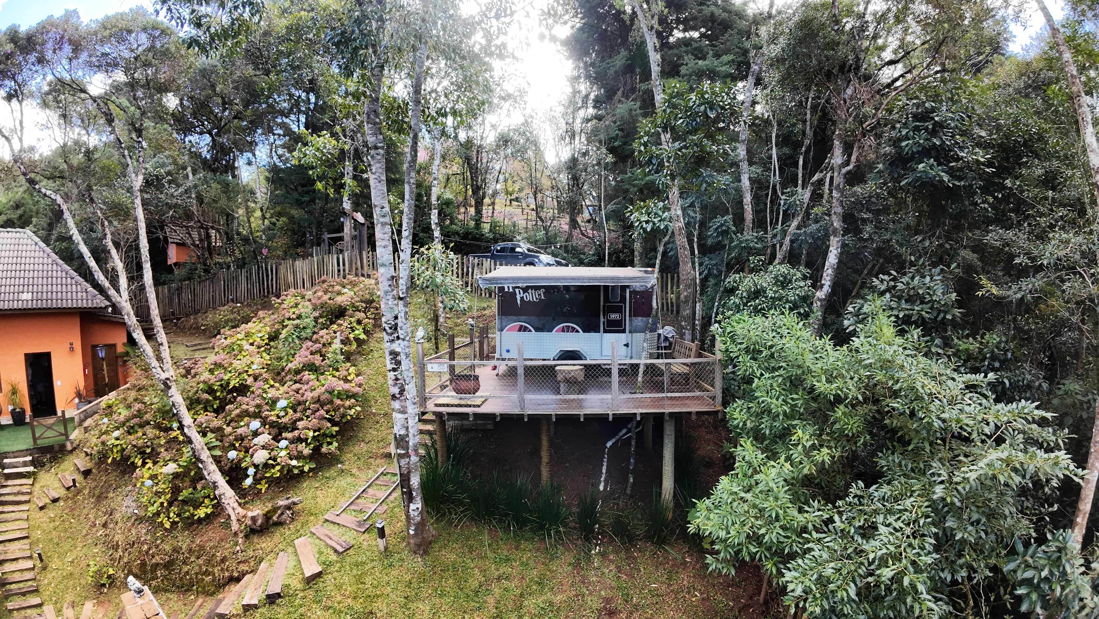 Ein Baumhaus mit einer kleinen Terrasse und einem überdachten Bereich, umgeben von dichtem Wald.