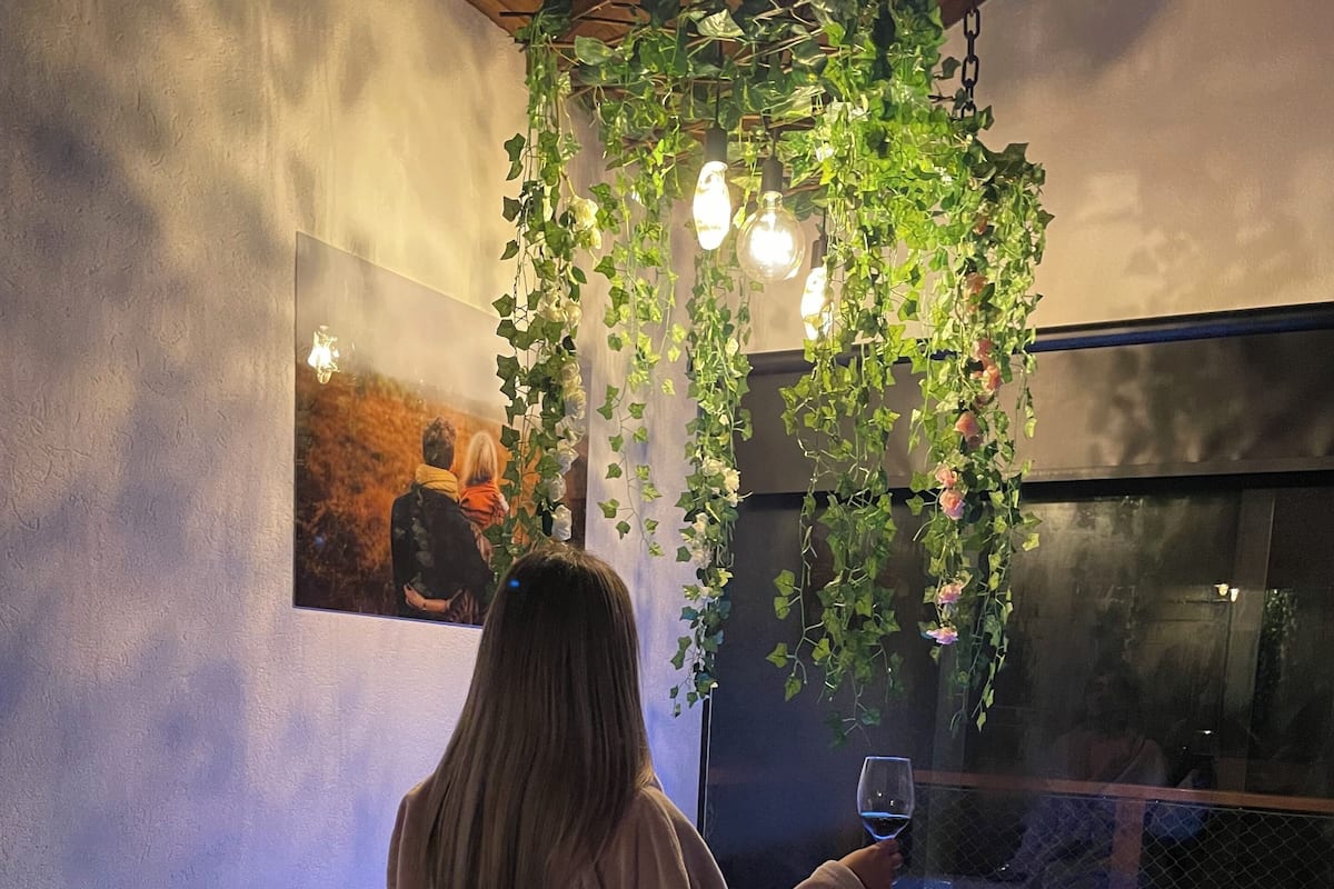 A person sitting in a bathtub with a blue light, surrounded by greenery and a framed picture on the wall.