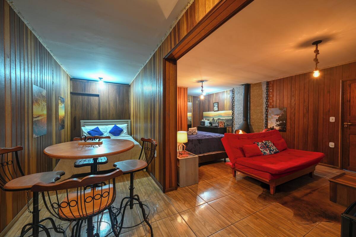 A cozy room with a wooden floor, a round dining table with chairs, a red sofa, and a bed with a blue headboard.