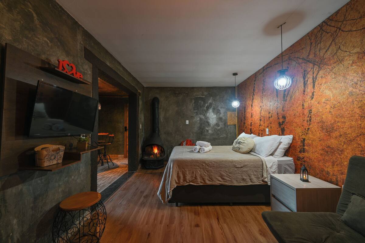 A modern bedroom with a large bed, a TV, a fireplace, and a unique wall mural.