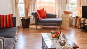 A modern living room with a grey sofa, red cushions, a coffee table with fruit, and a TV on a stand. - 1 Bed Studio Sleeps 4 - Seaside, Dog Friendly (Bridlington)