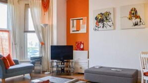 A modern living room with a flat-screen TV, grey sofa, and ottoman. - 1 Bed Studio Sleeps 4 - Seaside, Dog Friendly (Bridlington)