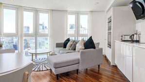Una sala de estar moderna con un sofá gris, una mesa redonda de cristal y vistas a la ciudad a través de amplias ventanas.
