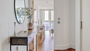 Un pasillo con un espejo, un florero con flores, una mesa de comedor con sillas y vistas a un balcón.