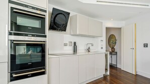 Una cocina moderna con hornos empotrados y un microondas, muebles de cocina blancos y suelo de madera.