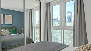 Un hotel moderno con una cama grande, una mesita de noche, un espejo y vistas de la ciudad a través de amplias ventanas.