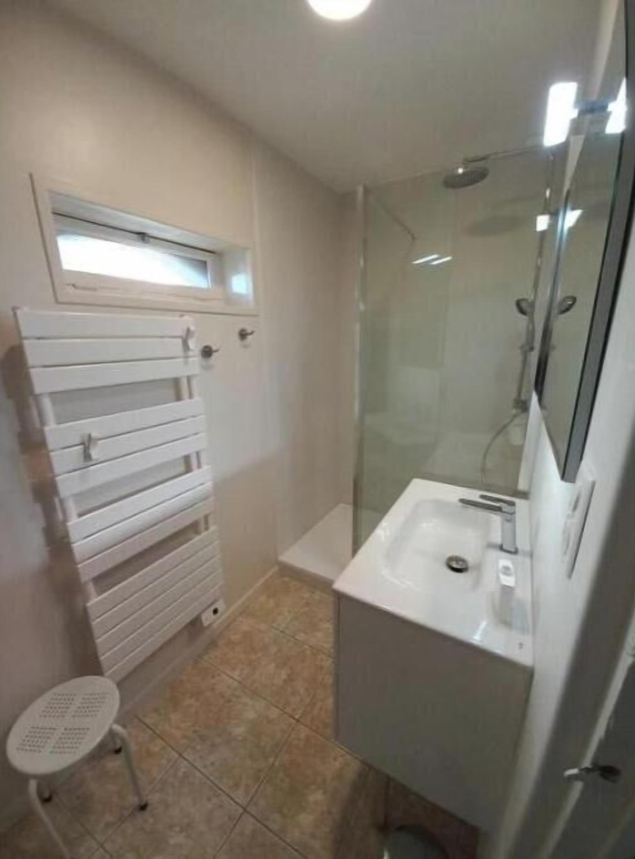 Een badkamer met een douche met glazen wanden, een witte wastafel en een handdoekhouder.