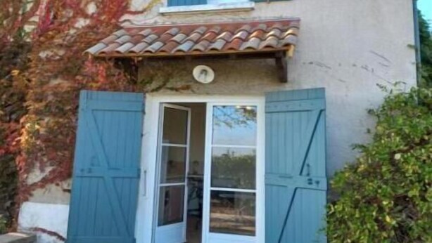 Un edificio de dos pisos con techo de tejas, una entrada central con puertas de vidrio y contraventanas azules en las ventanas.