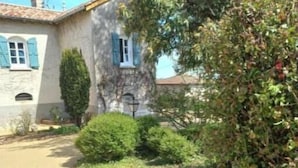 Un edificio rústico de piedra con camino de grava y abundante vegetación.