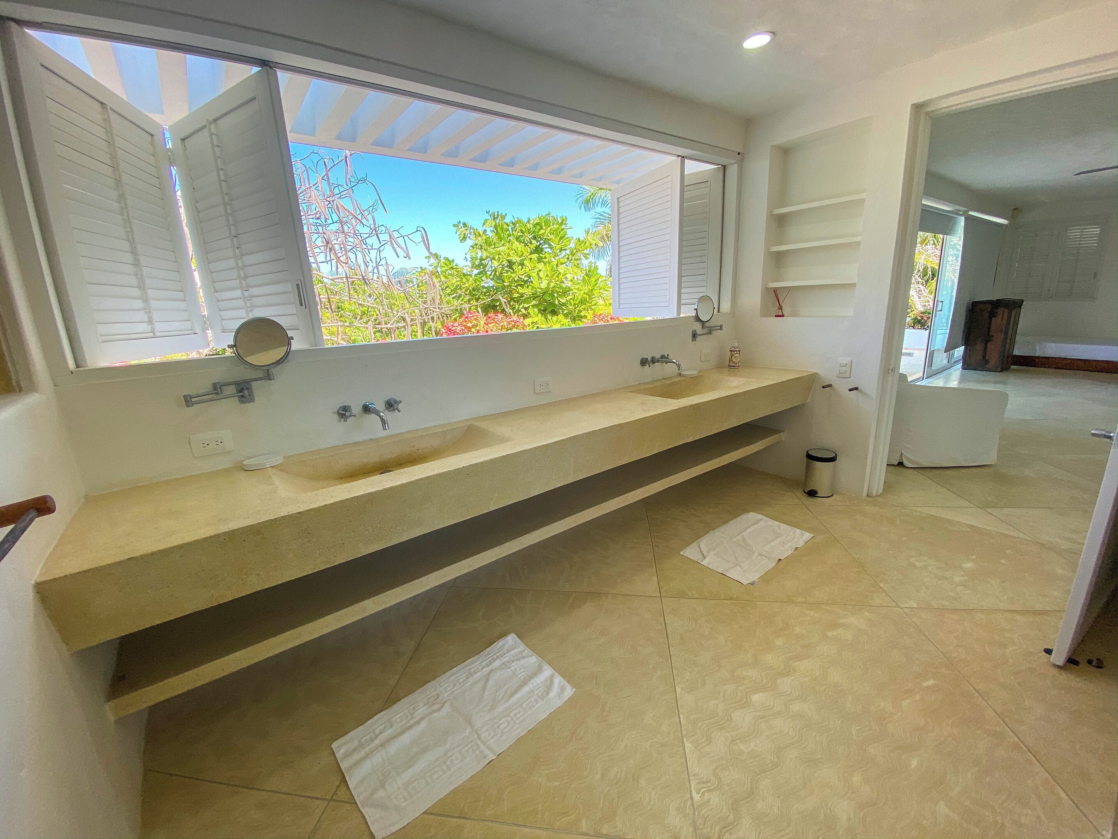 A bathroom with a large sink, a mirror, and a window with shutters.