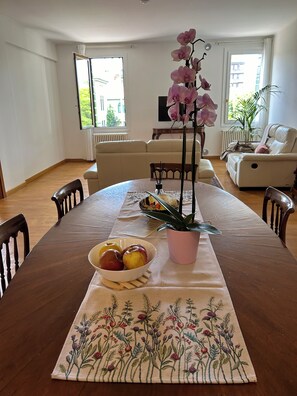 Et spiseområde med et træbord, stole, en skål med frugt, en pink orkidé og en potteplante.