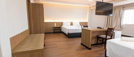 A hotel room with a bed, a desk, a chair, a TV, and a window with curtains.