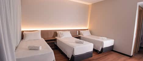 Habitación de hotel con tres camas individuales, suelo de madera y diseño moderno.