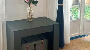 Una habitación con una mesa de madera oscura, un reloj en la pared, un jarrón con flores y una ventana con cortinas.