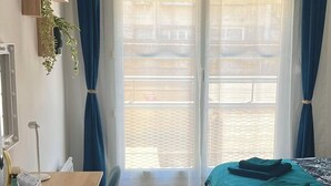 Habitación con cama, escritorio y silla. Hay cortinas, una planta y una ventana.
