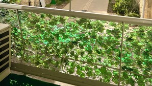 Un balcón con vista a una calle, una cerca verde y un edificio con ventanas.
