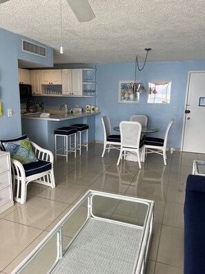 A modern kitchen with white cabinets, a microwave, and a sink. There are two white wicker chairs and a small round table with a white tablecloth. - 2Bed 2Bath Marbella 15th Floor Condo with STUNNING Beachfront Views, WasherDryer (Carolina)