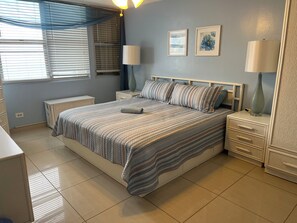 A bedroom with a bed, nightstands, a lamp, a bedside table, a window with blinds, and a wall with two framed pictures. - 2Bed 2Bath Marbella 15th Floor Condo with STUNNING Beachfront Views, WasherDryer (Carolina)