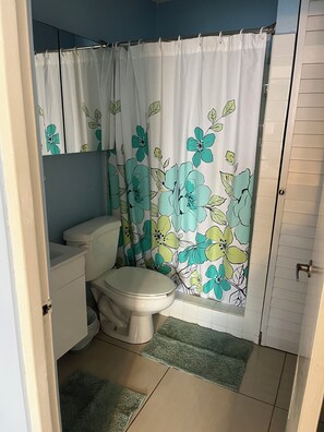 A bathroom with a toilet, a shower curtain with floral patterns, and a green rug. - 2Bed 2Bath Marbella 15th Floor Condo with STUNNING Beachfront Views, WasherDryer (Carolina)