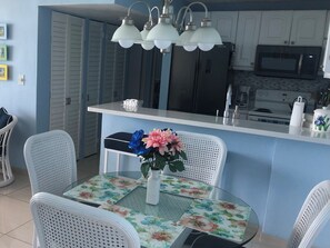 A kitchen with white cabinets, a microwave, and a sink. There is a dining table with chairs and a vase with flowers. - 2Bed 2Bath Marbella 15th Floor Condo with STUNNING Beachfront Views, WasherDryer (Carolina)