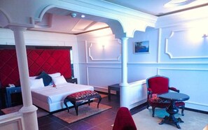 A hotel room with a bed, a red upholstered chair, a small round table, and a decorative wall panel.