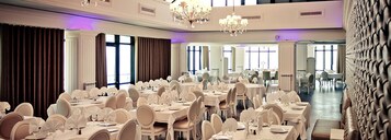 Un salón de banquetes con varias mesas redondas, sillas blancas y candelabros.