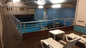 Zona de piscina amb terrassa de fusta, baranes metàl·liques i una taula petita amb cadires.