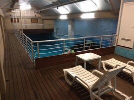 Zona de piscina con terraza de madera, barandas metálicas y una pequeña mesa con sillas.