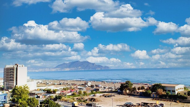 Paisatge urbà costaner amb platja, edificis i muntanyes a la distància.