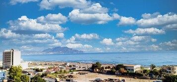 Un paisaje costero con playa, edificios y montañas al fondo.