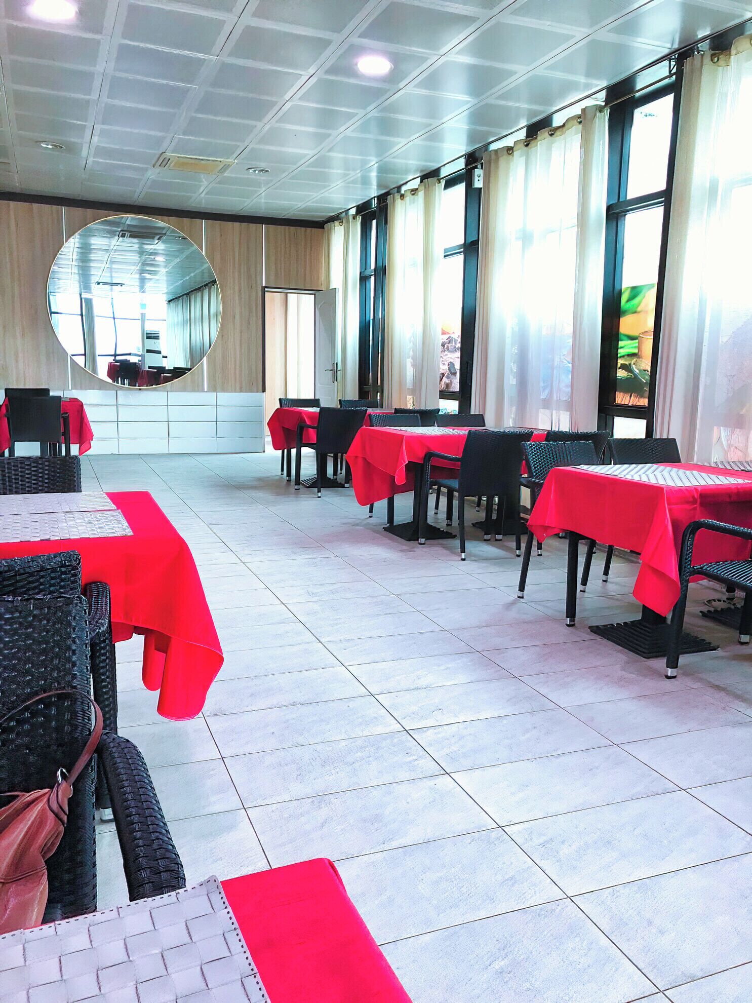 Un restaurante con varias mesas cubiertas con manteles rojos, sillas negras y un espejo grande en la pared.