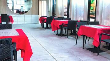 Un restaurante con varias mesas cubiertas con manteles rojos, sillas negras y un espejo grande en la pared.