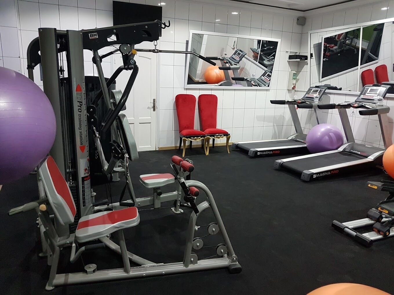Et fitnesscenter med træningsudstyr, løbebånd og røde stole.