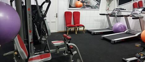Et fitnesscenter med træningsudstyr, løbebånd og røde stole.