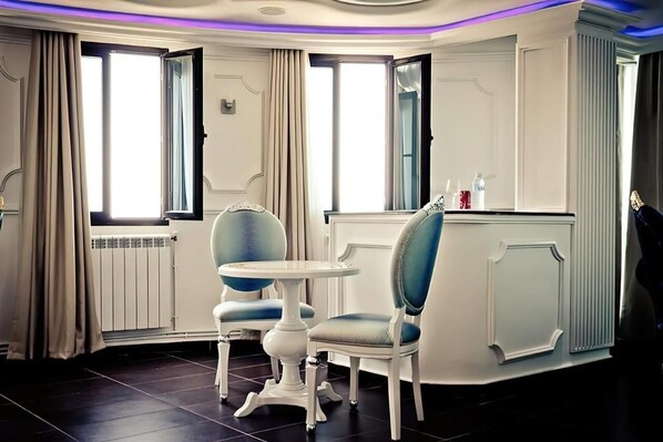A room with two chairs and a small table, a radiator, and a window with curtains. - Raya Tichy (Tichy)