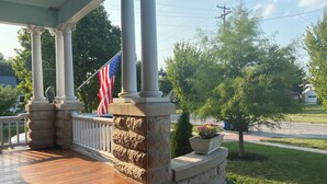 A covered porch with stone columns, a flag, and a small tree with flowers. - THE VICTORIAN GUESTHOUSE BED & BREAKFAST - Room 3 (Delphos)
