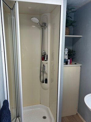 Et lille, lukket bruseområde med en håndholdt bruser, en indbygget siddeplads og en hylde med toiletartikler.