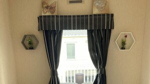 Une chambre avec deux lits, chacun recouvert d’une courtepointe blanche ornée de motifs de flamants roses, une table centrale et une fenêtre avec des rideaux.
