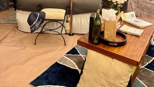 A cozy tented accommodation with a bed, bedside table, lamp, and a small table with a bottle and papers. - Stunning 1-bed Glamping Tent in Cleveland (Conroe)