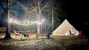 A tent set up in a forested area with a hammock and picnic table nearby. - Stunning 1-bed Glamping Tent in Cleveland (Conroe)