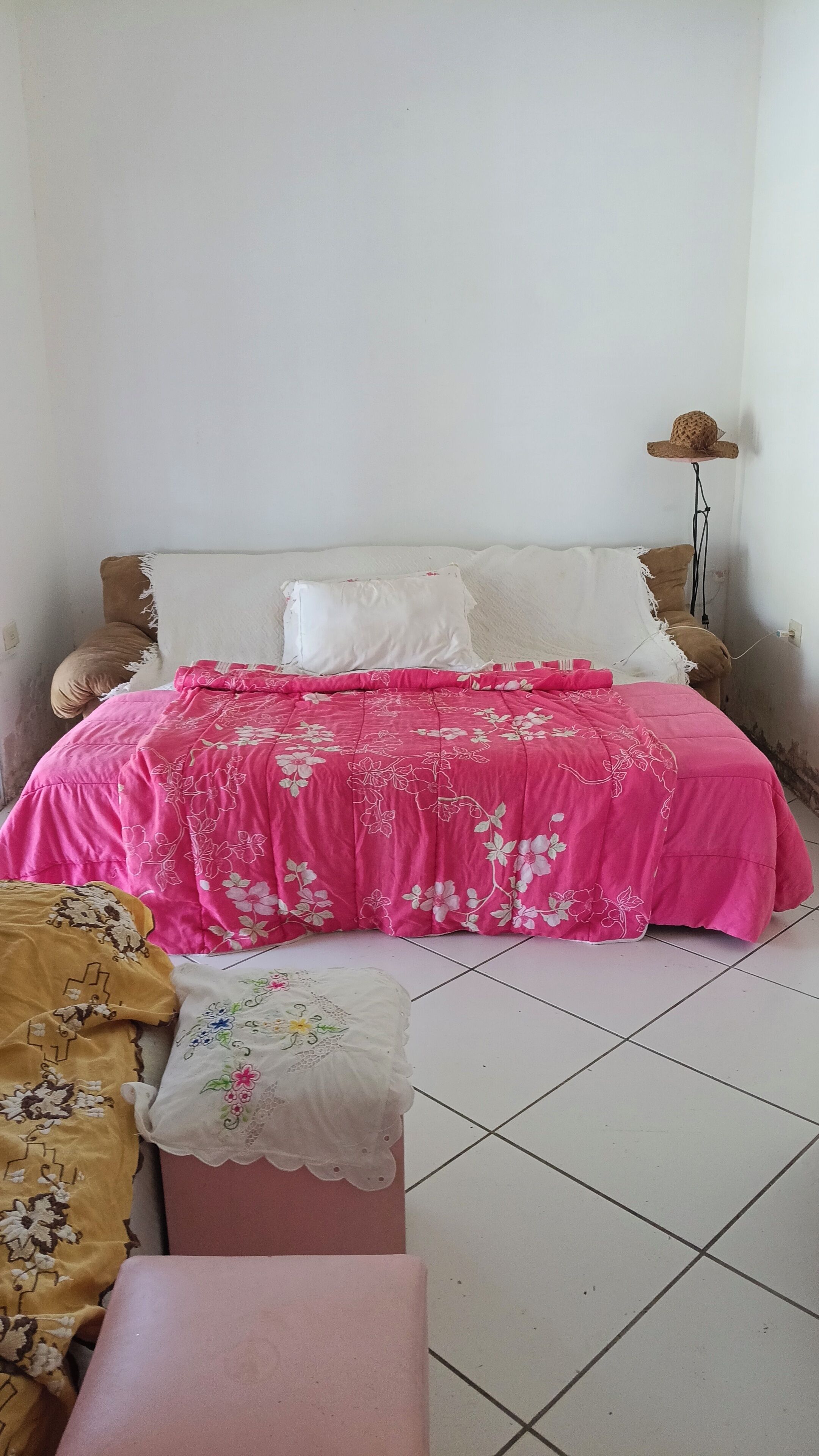 A bed with a pink floral bedspread, a white pillow, and a brown pillow.