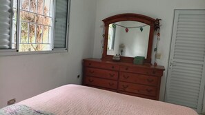 Ein Schlafzimmer mit Bett, Kommode, Spiegel und Fenster.