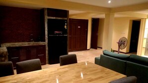 Un comedor con una mesa y sillas de madera, una pared de ladrillo, un refrigerador negro y un sofá verde.
