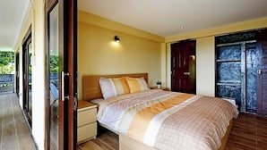 Un dormitorio con una cama grande, una mesita de noche, una lámpara de pared y un ventanal corredero que da a un área exterior.
