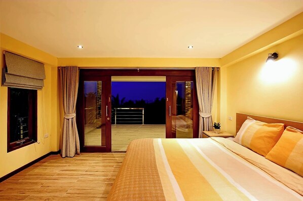 Un dormitorio con una cama grande, una puerta corrediza de vidrio a un balcón y vistas al cielo nocturno.