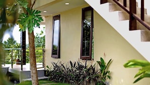 Una casa moderna con una escalera que conduce a un balcón, rodeada de abundante vegetación y plantas en macetas.