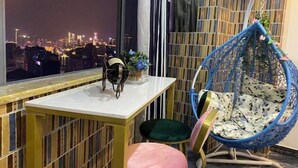 Un balcon offrant une vue sur le paysage urbain nocturne, un fauteuil suspendu, une petite table avec une chaise et une plante décorative.