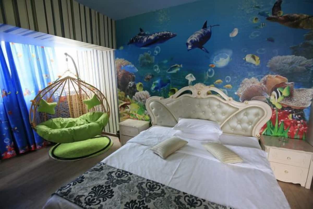 A bedroom with a bed, a hanging chair, and a mural of underwater scenery.