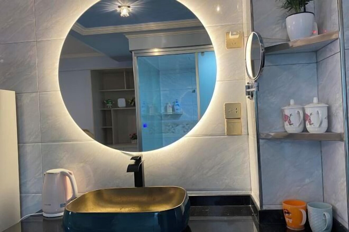 A bathroom with a round mirror, a sink, a shower, and shelves with toiletries.