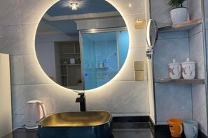 A bathroom with a round mirror, a sink, a shower, and shelves with toiletries.